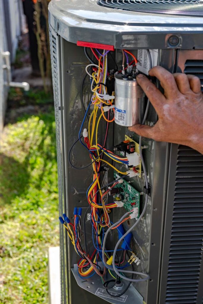 A Custom Air Conditioning & Air Quality technician inspects the internal wiring and components of an outdoor air conditioning unit ensuring proper AC service and repair