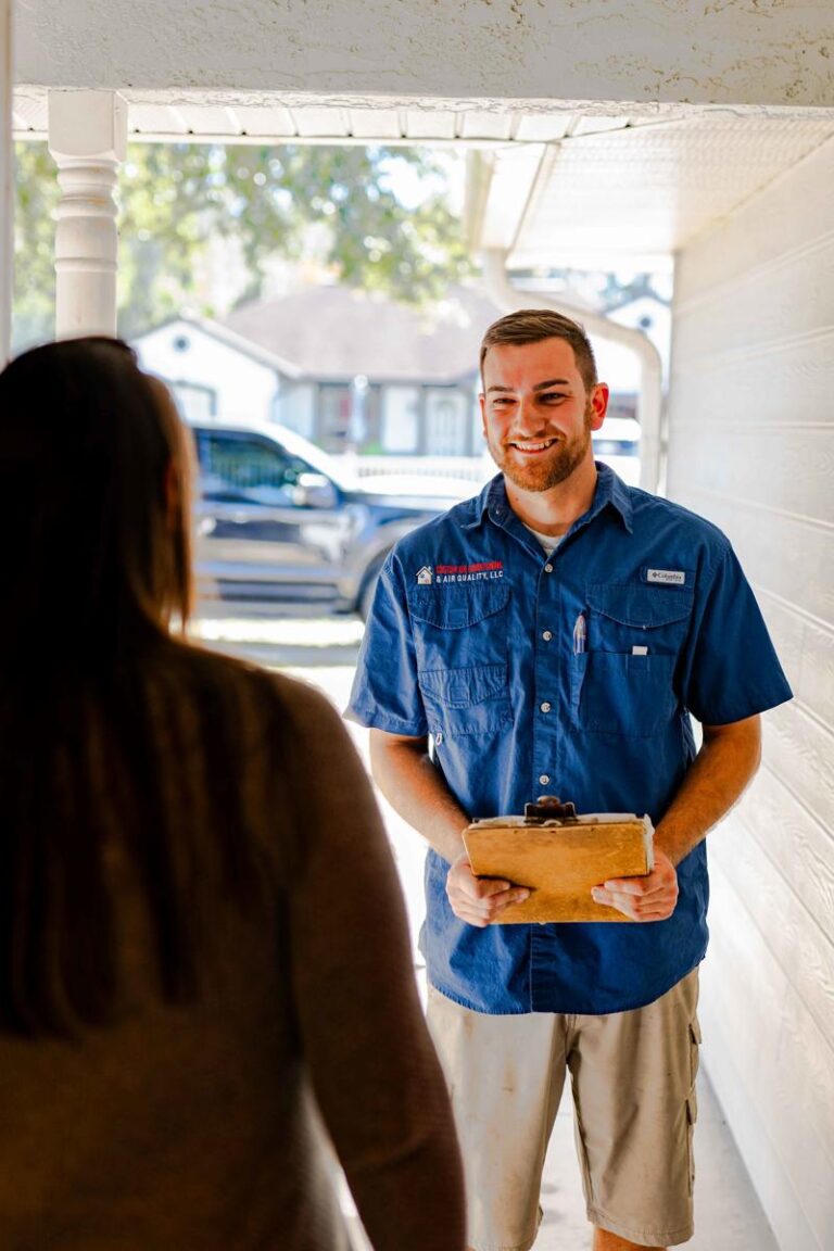 A Custom Air Conditioning & Air Quality technician smiles while speaking with a customer at her front door holding a clipboard during a service visit