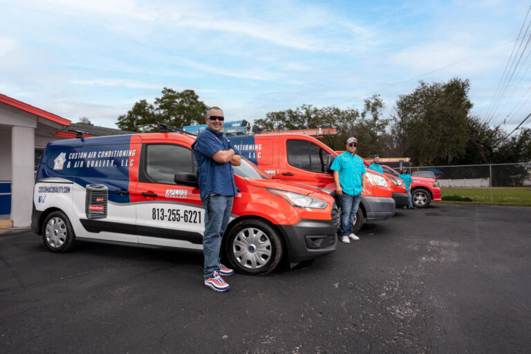 Custom Air Conditioning & Air Quality team members stand proudly beside their branded service vans parked outside the company’s office ready for AC repair and service calls