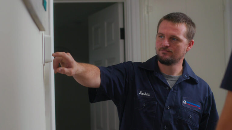 Custom air conditioning and air quality technician adjusting a thermostat for optimal cooling